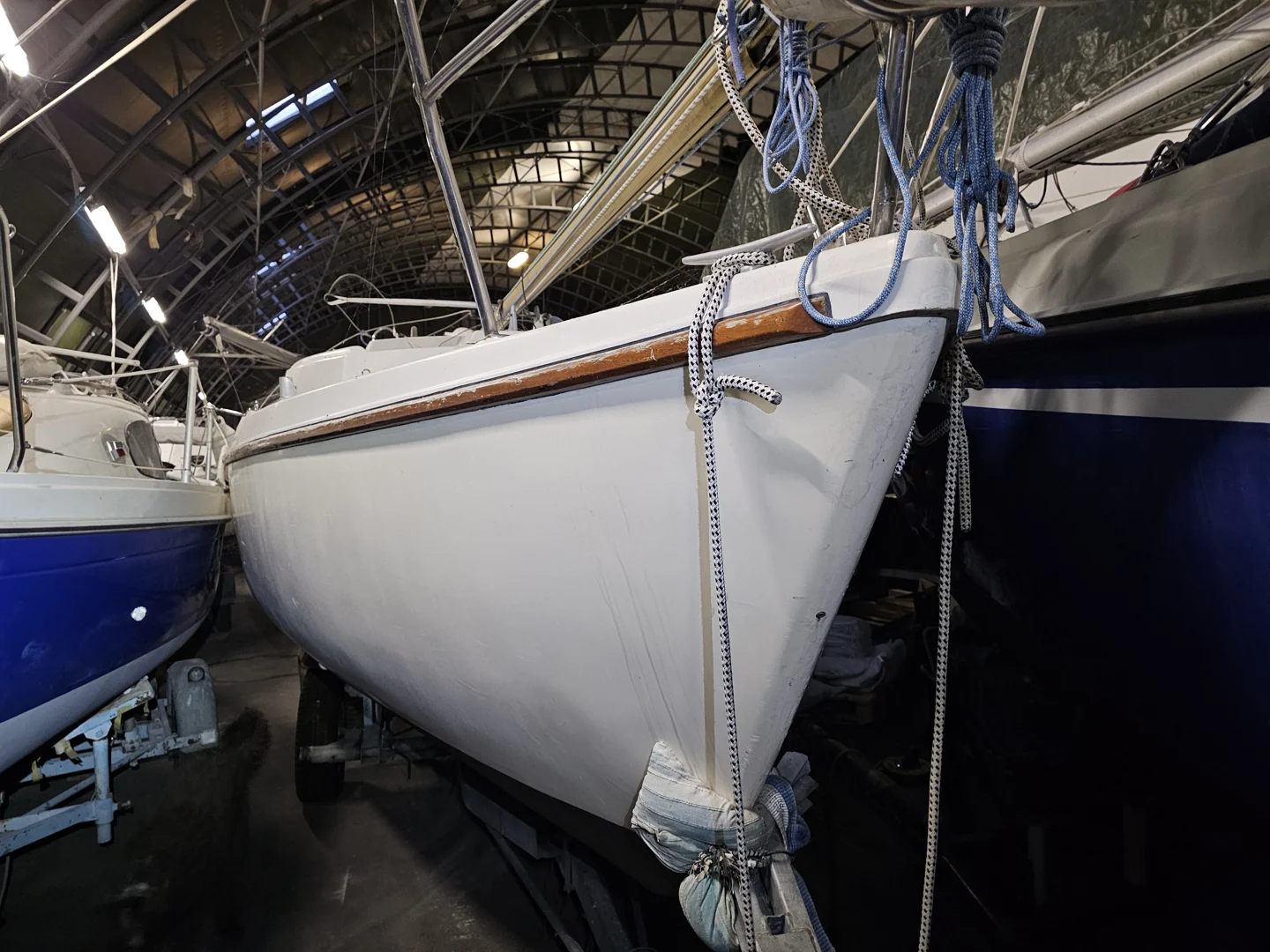 Originalaufnahme eines älteren Segelbootes mit Gebrauchsspuren an Rumpf und Holzleiste im Winterlager