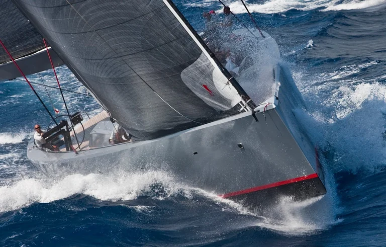 Sportliche graue Segelyacht unter Segeln mit Gischt am Bug